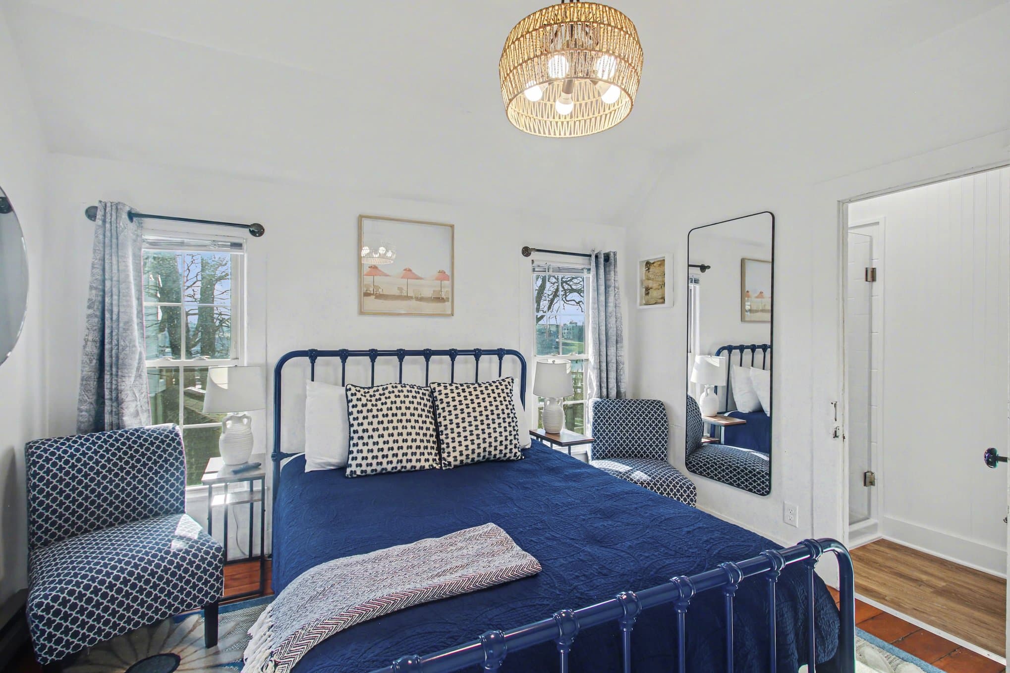 Queen bed with blue headboard between two bright windows