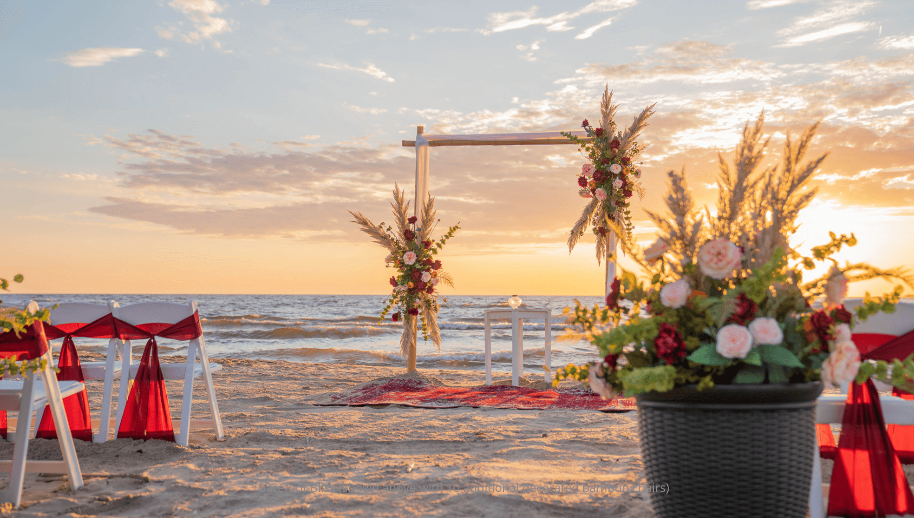 A beautifully decorated beach wedding setup with floral arrangements under a sunset sky.