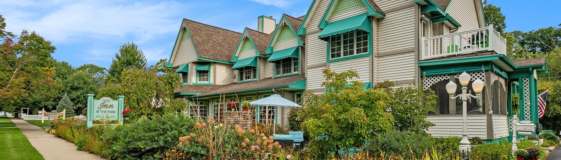 Victorian-style house with teal accents surrounded by gardens on a sunny day.