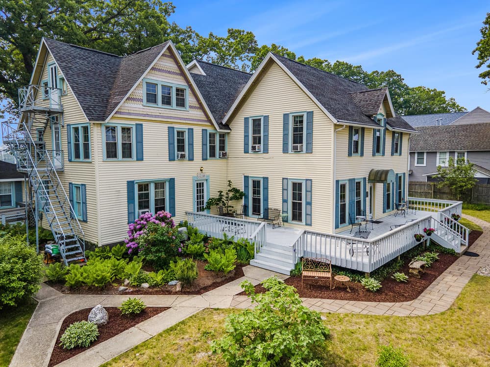 A large, two-story house with blue shutters, surrounded by a landscaped garden and a patio. A large, two-story house with blue shutters, surrounded by a landscaped garden and a patio.