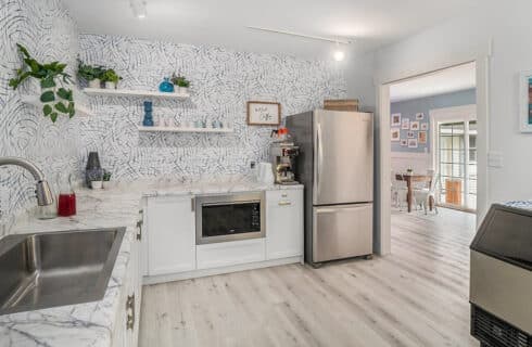 A modern kitchen featuring white cabinetry, marble countertops, and patterned wallpaper.