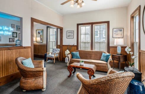 A cozy living room with wicker furniture and large windows.