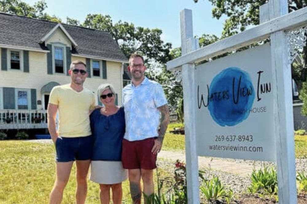 Three people stand in front of a house holding a sign for Waters View Inn.