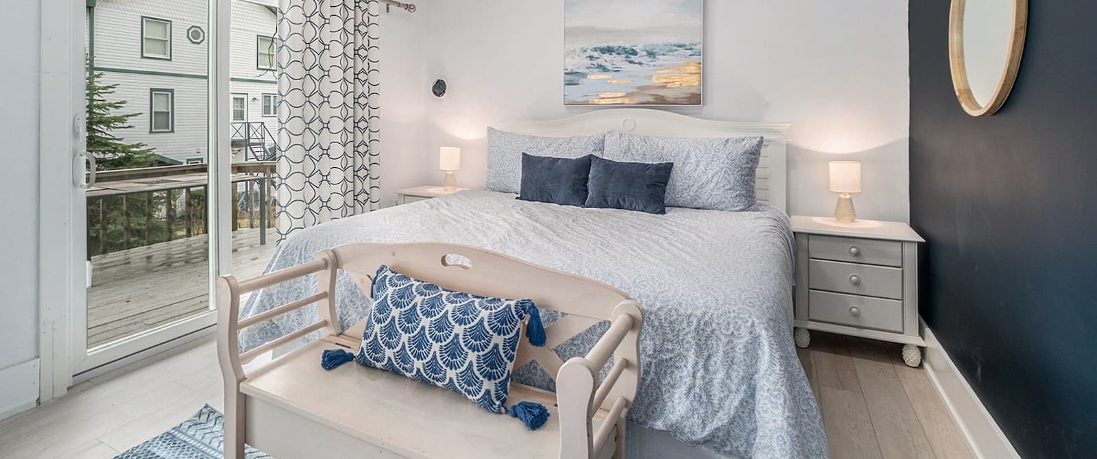 A cozy bedroom featuring a large bed with decorative pillows, a small bench at the foot, and a sliding door leading to a balcony.