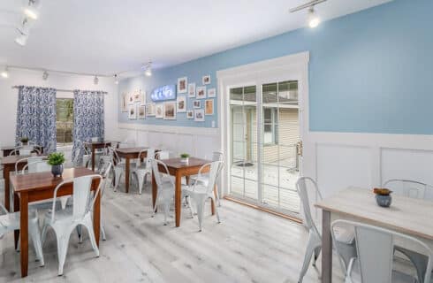 Bright and airy café interior with wooden tables and metal chairs, featuring blue walls and large windows.