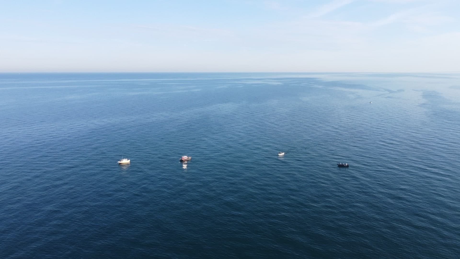 A serene ocean view with four boats floating on calm waters under a clear blue sky. A serene ocean view with four boats floating on calm waters under a clear blue sky.