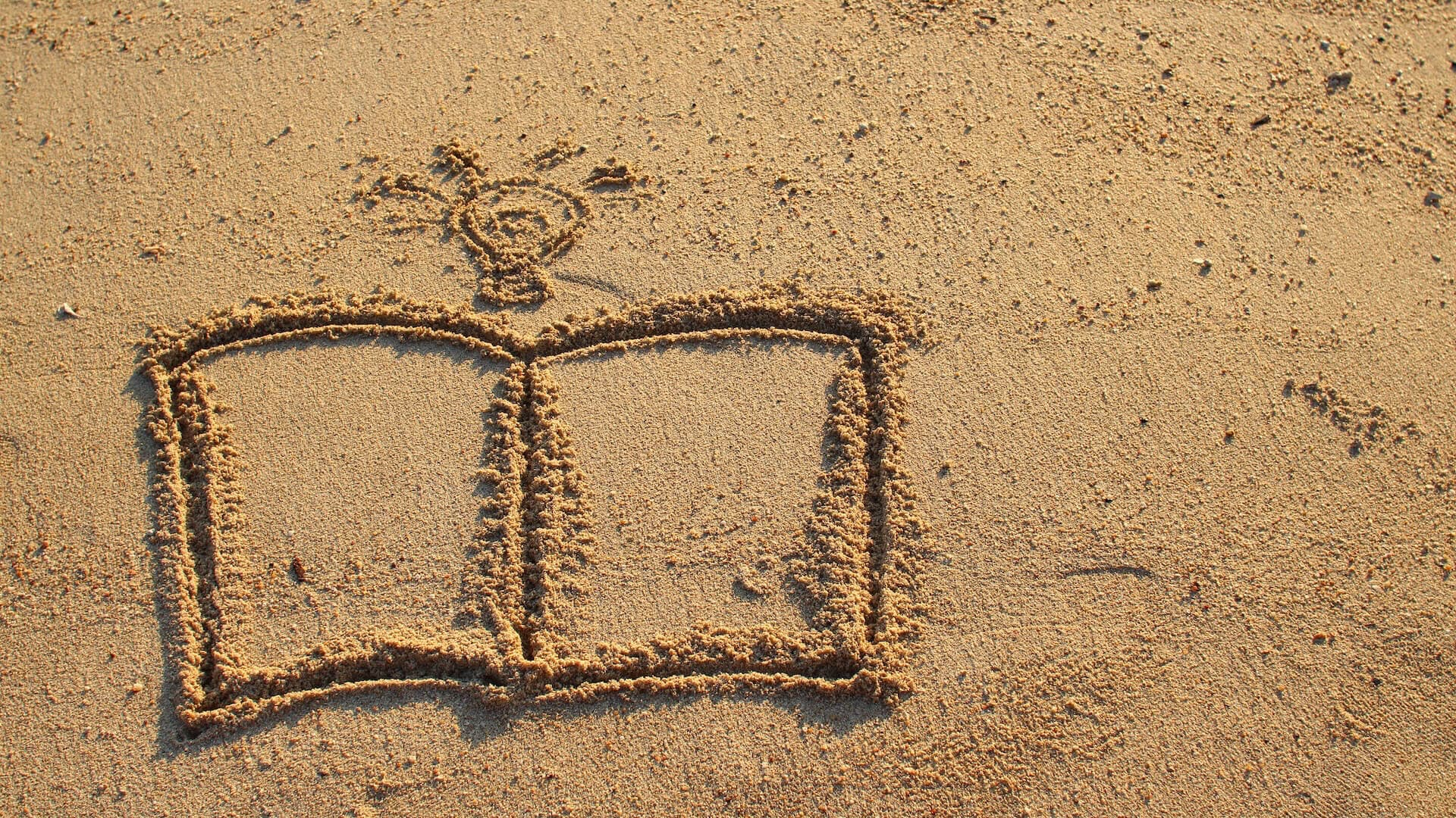 A book shape drawn in sand with a sun illustration above it.