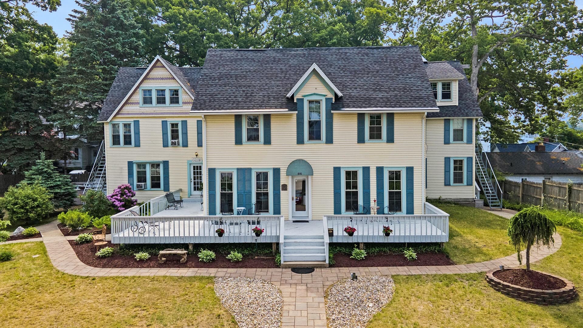 A large, yellow Victorian-style house with blue shutters and a porch, surrounded by a well-maintained yard.