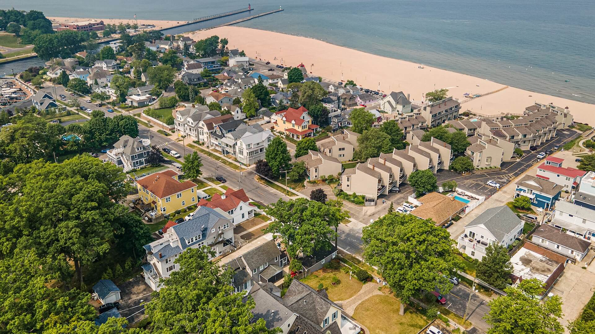 Aerial view of a coastal town with residential streets, greenery, and a sandy beach.