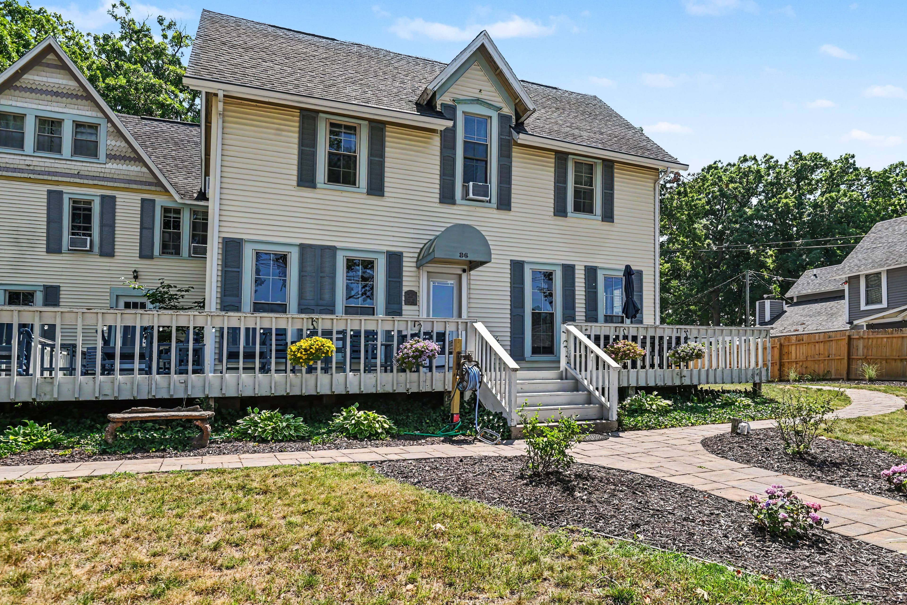 Two-story yellow house with blue shutters and a front porch, surrounded by a landscaped yard.