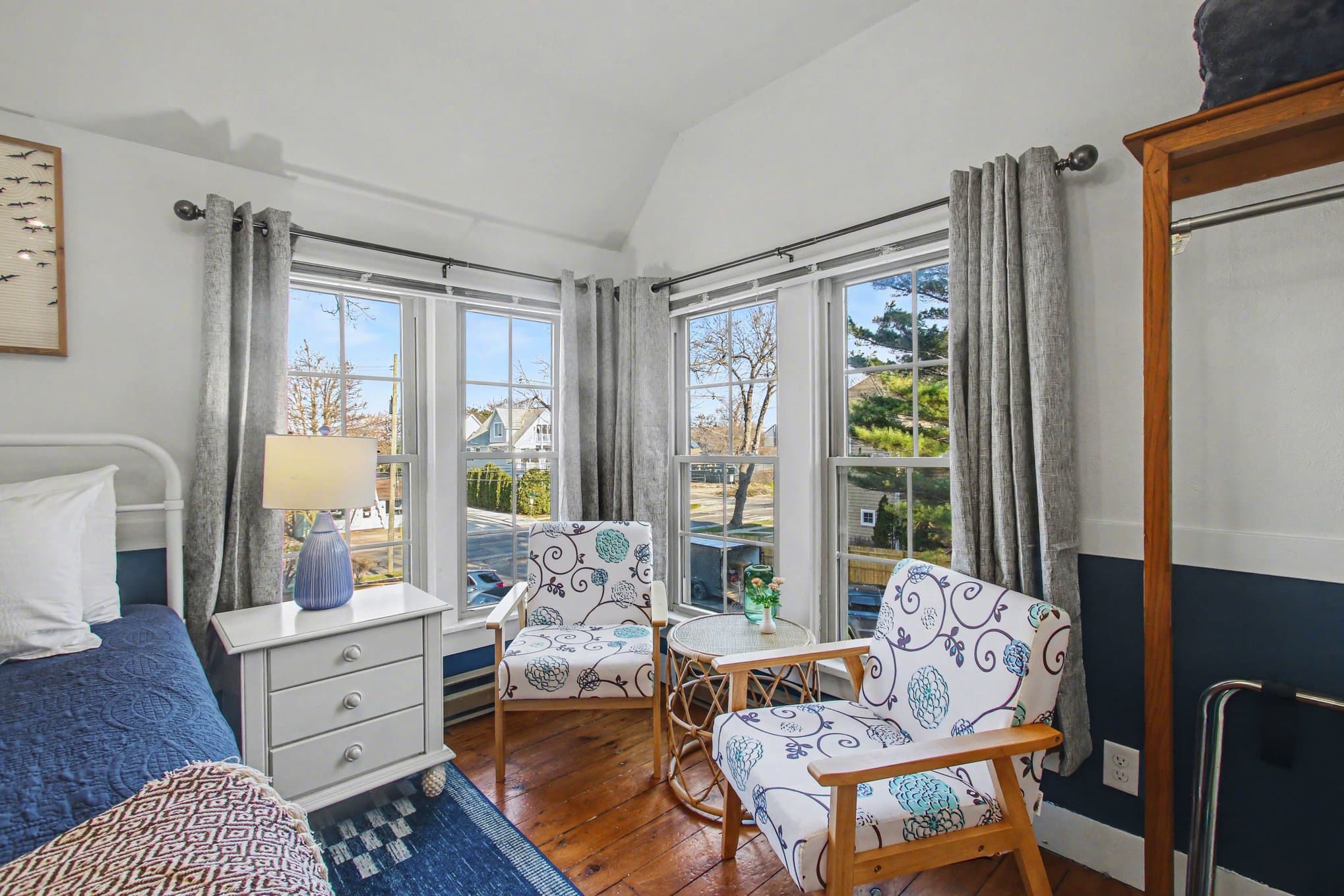 Cozy bedroom with a blue and white color scheme, two stylish chairs, and large windows letting in natural light.