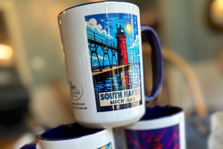 A stacked arrangement of mugs featuring a colorful illustration of a lighthouse and the text "South Haven, Michigan."