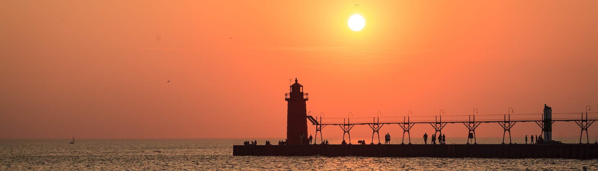 A sunset view of a lighthouse on a pier