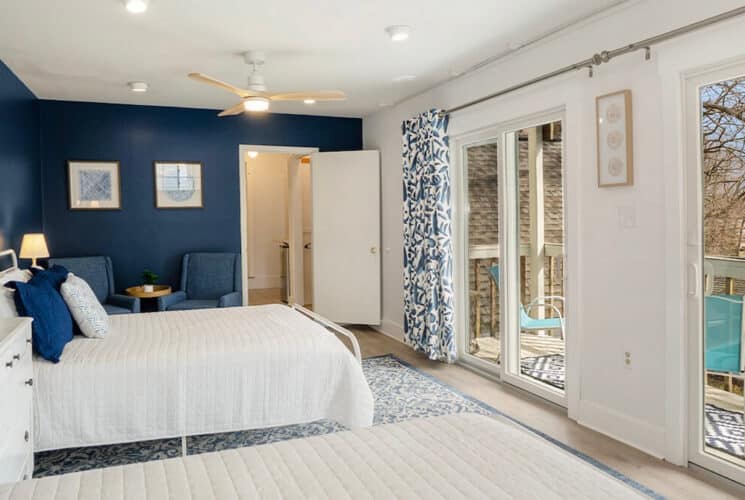 A spacious bedroom with dark blue and white walls, a bed with white and blue bedding, a white dresser, and sliding doors out to a private deck.