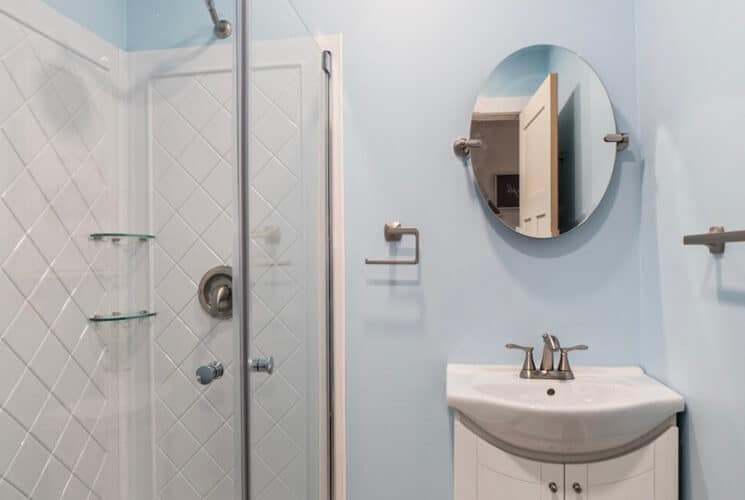 A bathroom with pale blue walls, a walk in shower, and wide sink with a mirror on the wall above it.