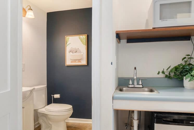 A bathroom with blue and white walls, and an area in the bedroom with a bar sink, microwave, and mini refrigerator.