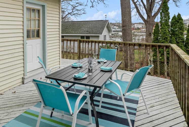An outdoor deck with a wood table and 4 blue patio chairs and a table set for 4.