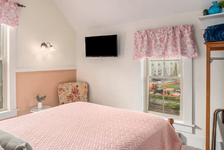 A bedroom with a bed with pink bedding, windows with pink valances, and pink and white walls.