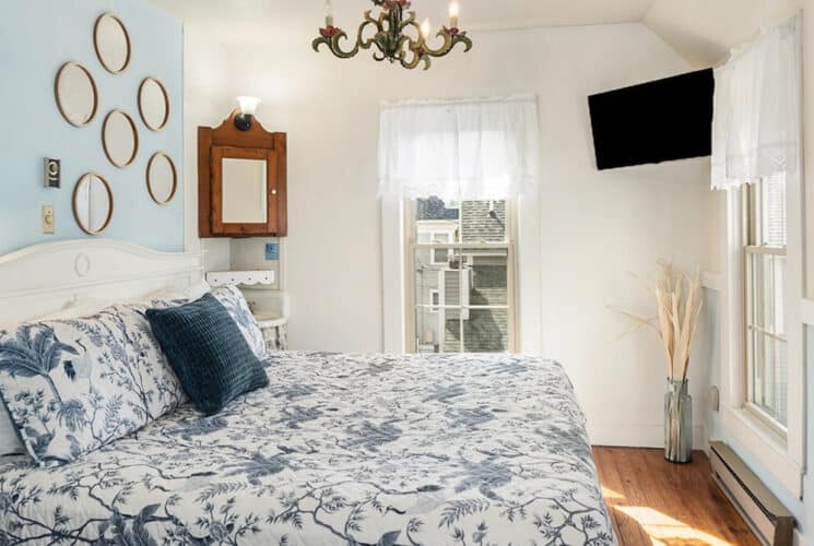 A bedroom with light blue and white walls, a bed with blue and white bedding, and a flat screen TV on the wall in the corner.