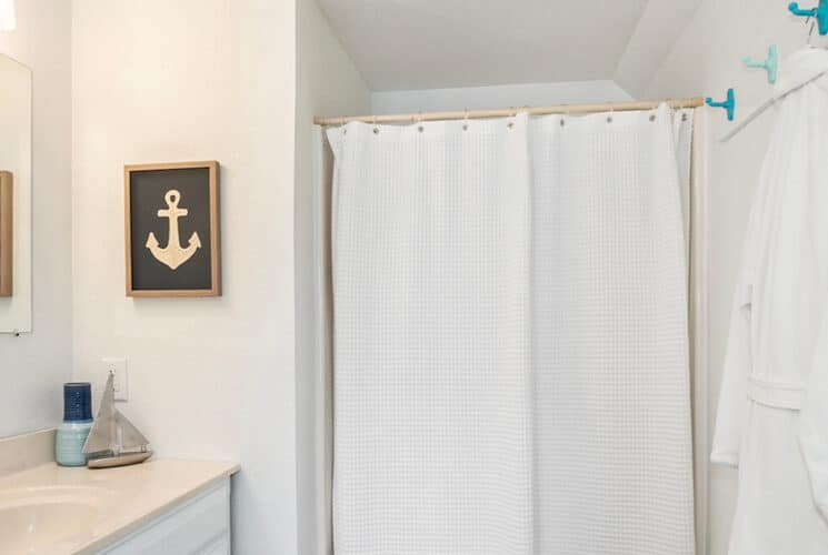 A bathroom with a walk in shower, a single sink, and a bathrobe hanging from a hook.