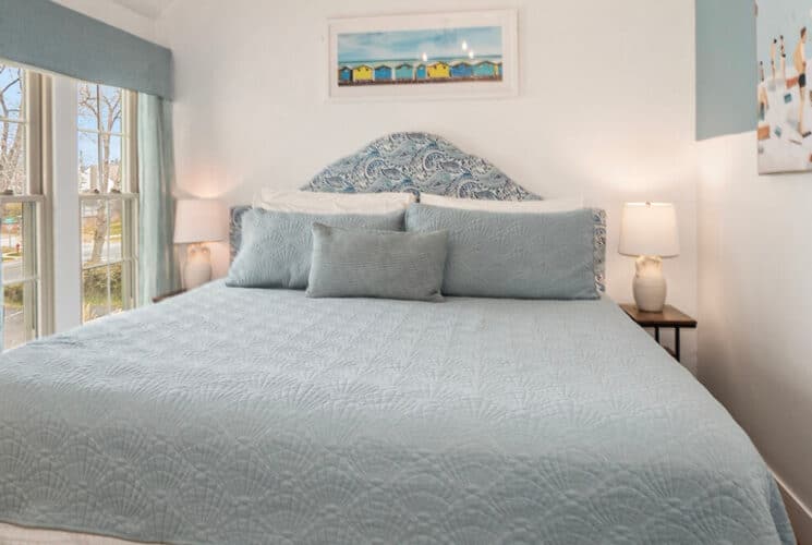 A bedroom with white walls, a bed with light bue bedding, sliding doors leading outside with light blue curtains.