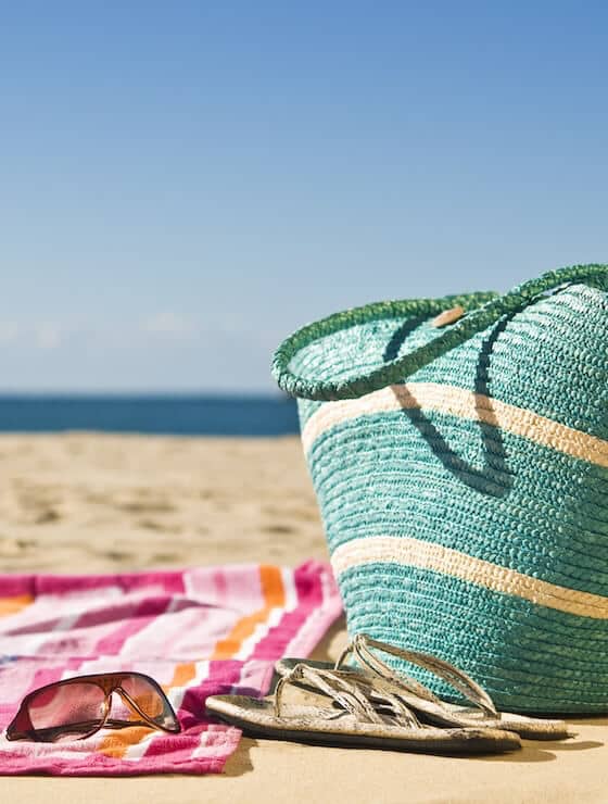 Vibrant towel, beach bag, sunglass and sandals spread out on the sand at the beach.