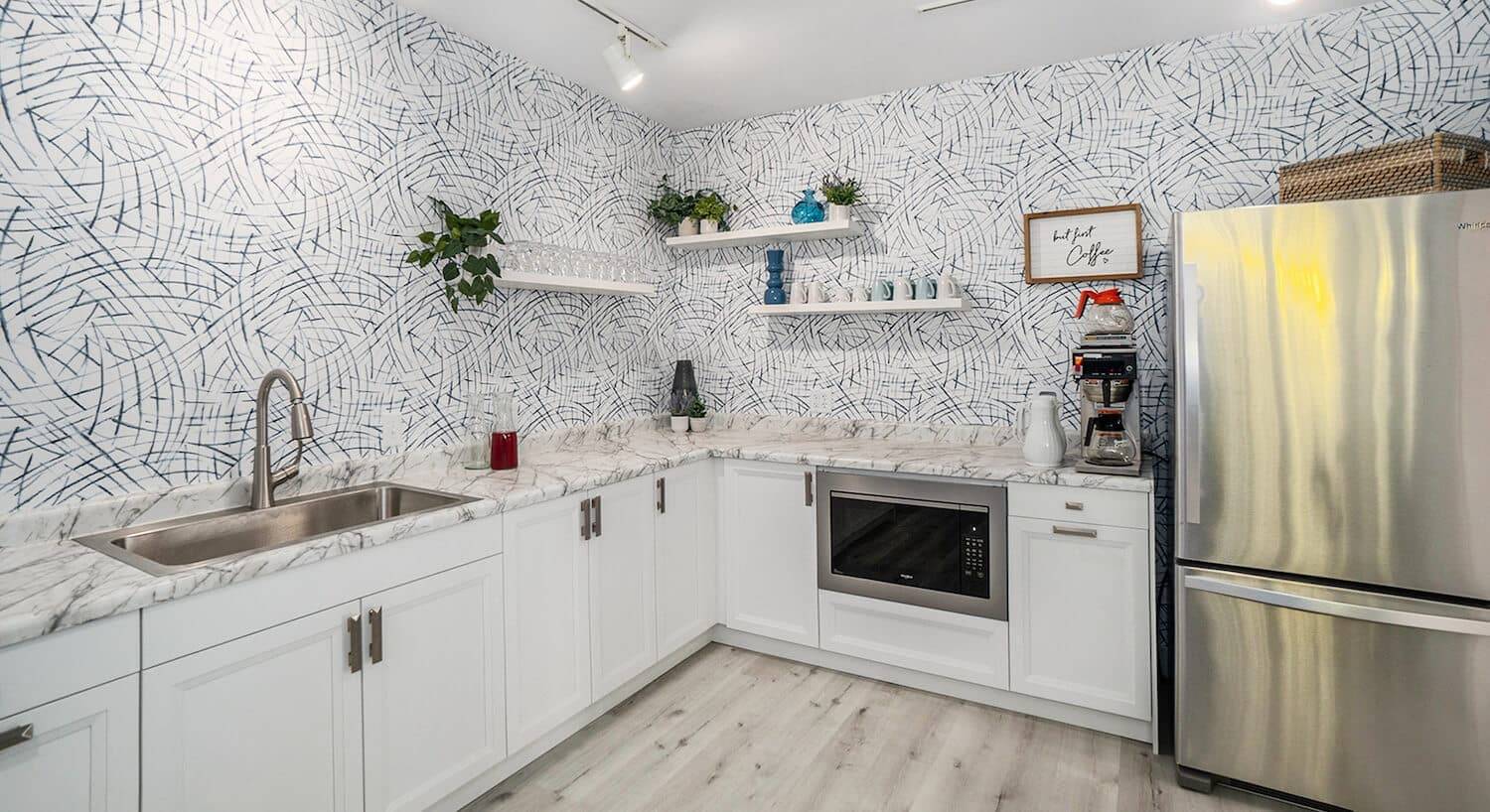 A kitchen with blue and white wallpaper, white cupboards, granite countertops, and stainless steel appliances
